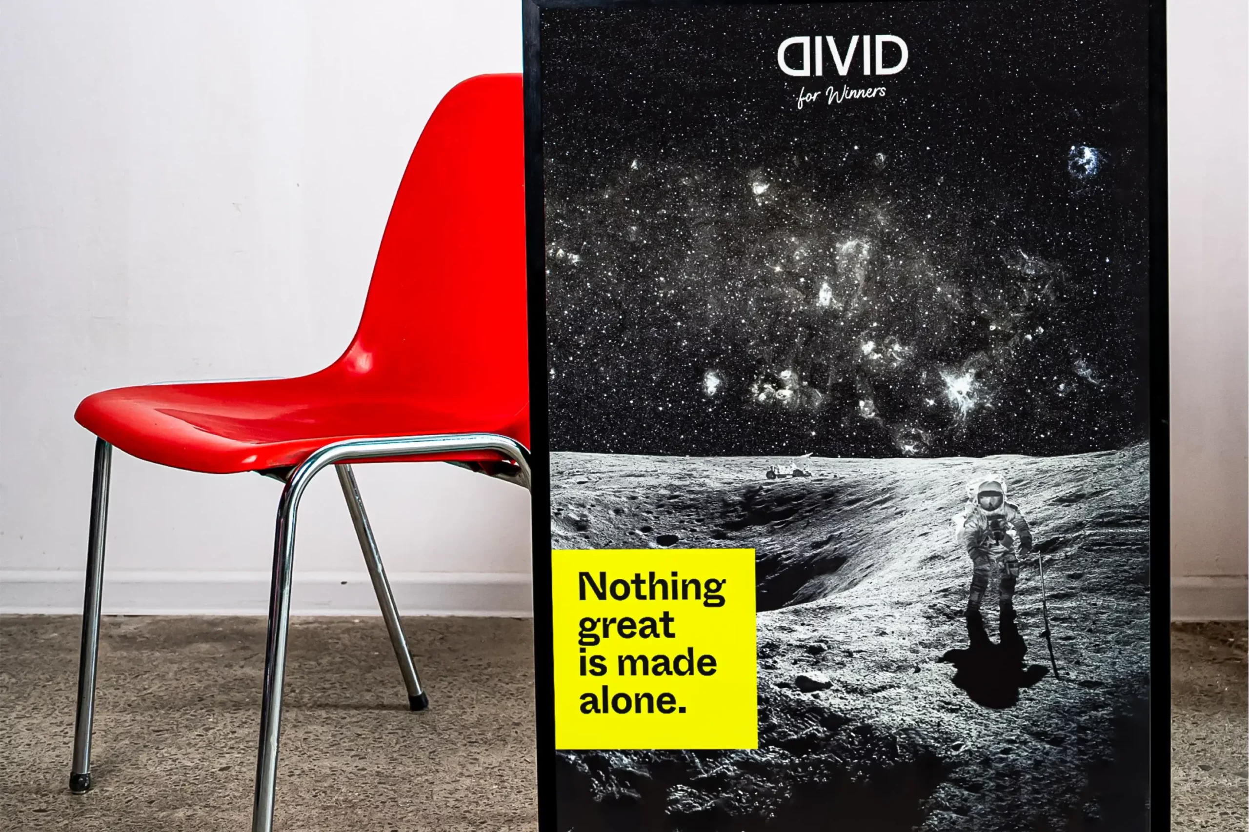 Divid: Poster «Nothing great is made alone» neben rotem Stuhl