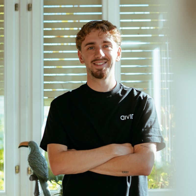 Nico Krüsi, Marketing Lead bei Divid in St. Gallen, steht lächelnd mit verschränkten Armen vor einer Fensterfront
